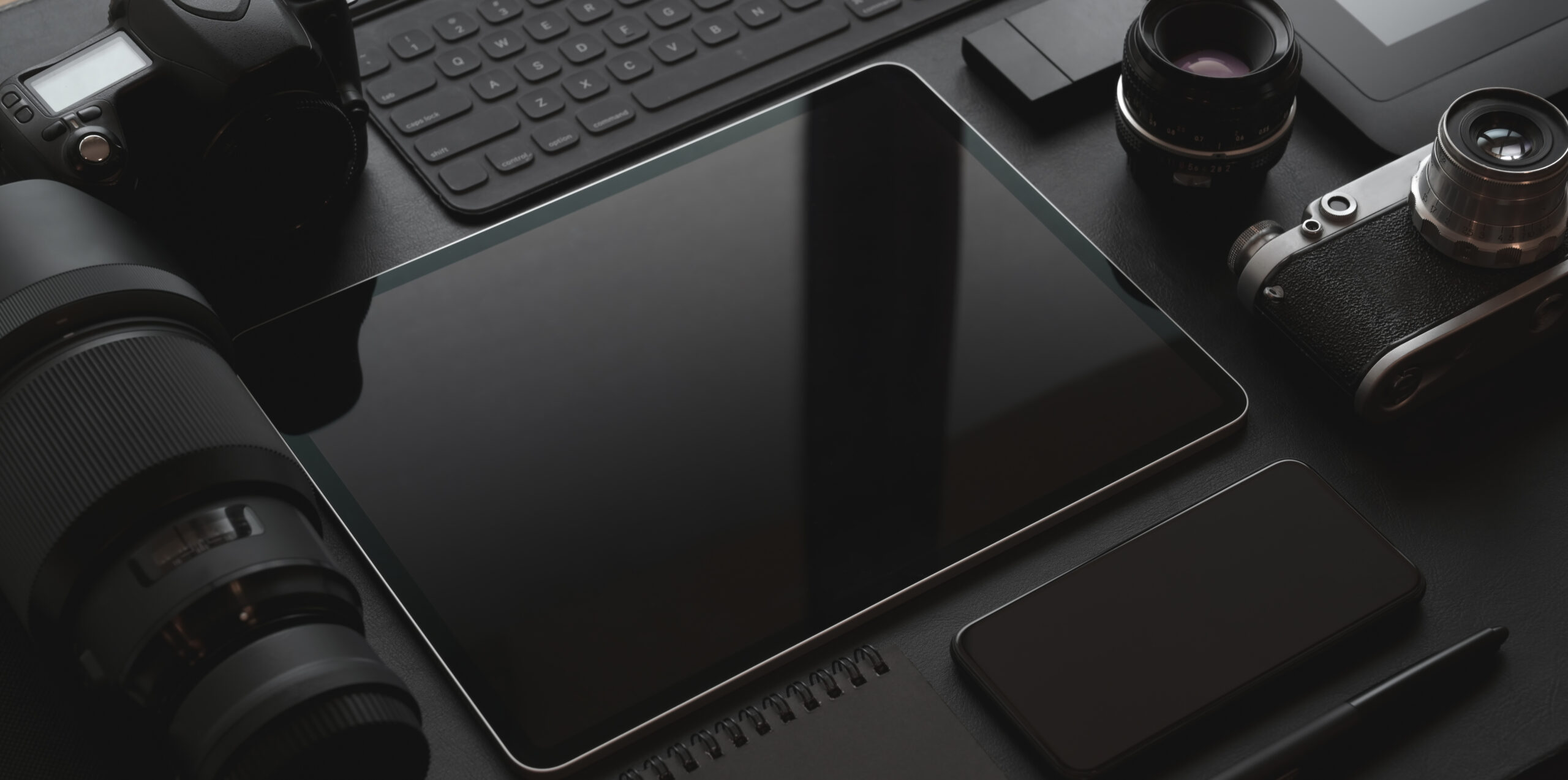 Dark trendy workplace with tablet, smartphone, camera and office supplies